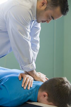 Chiropractor na may ginagawa sa leeg, at bahagi ng balikat ng lalaking nakahiga sa mesa.