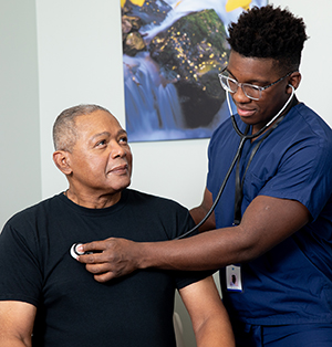 Healthcare provider listening to man's chest with stethoscope in exam room.